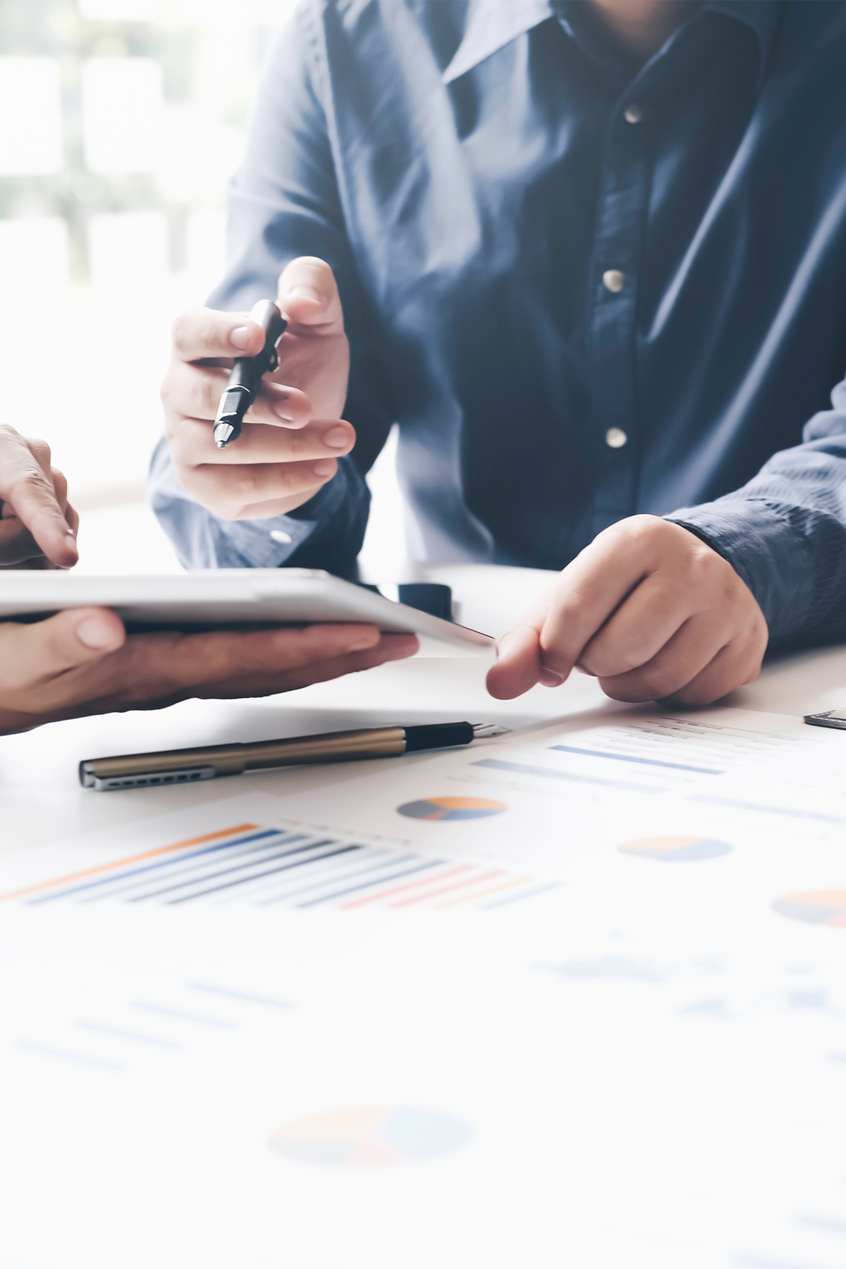 Zwei Personen in Geschäftskleidung überprüfen Datentabellen und Diagramme auf einem Tisch mit einem Tablet und Stiften.