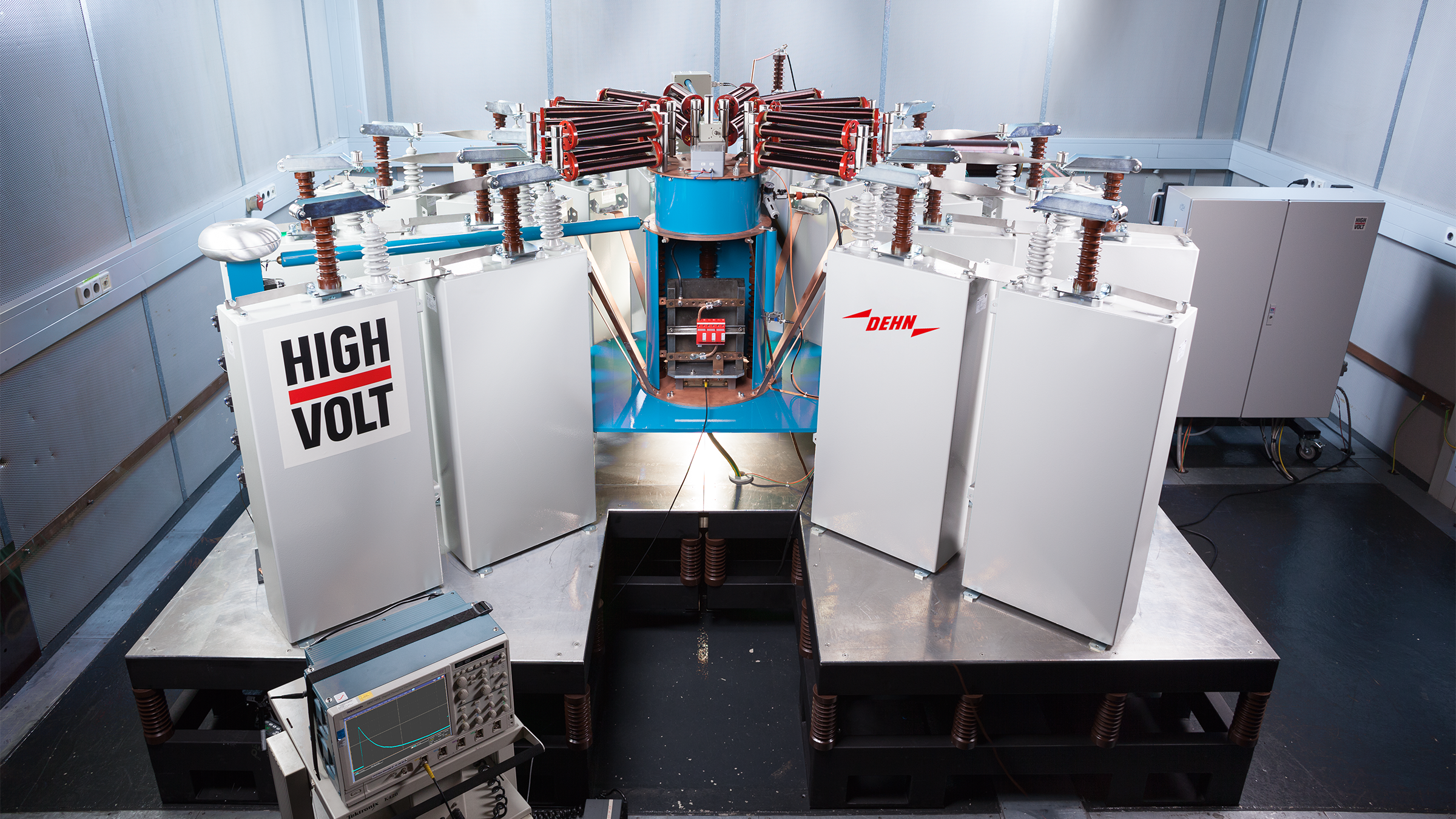 Hochspannungsprüfgerät mit mehreren isolierten Fächern und einem zentralen, blau-roten Bauteil in einer Laborumgebung.