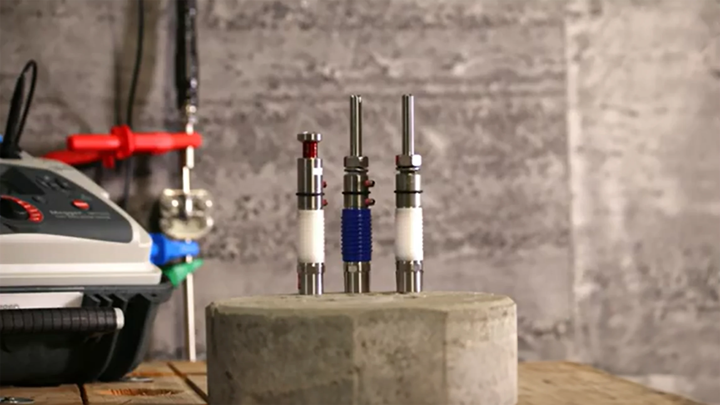 Three metal probes with insulating sleeves inserted vertically into a concrete block on a wooden surface.