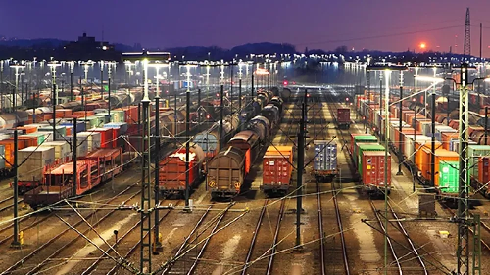 Bahnhofgelände mit vielen Gleisen, Weichen und Stromleitungen vor der Silhouette einer Stadt.