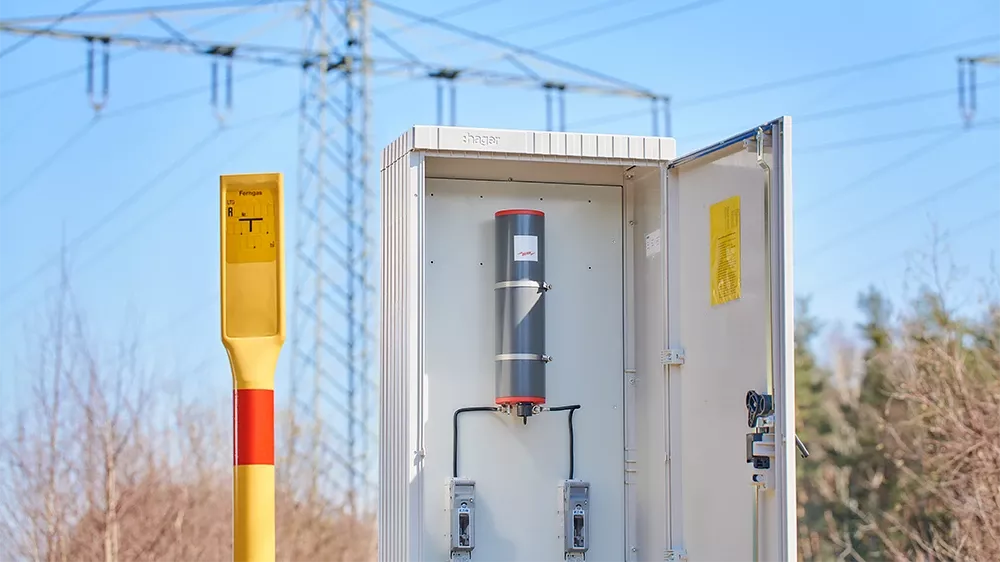 Abgrenzeinheit im geöffneten Schutzgehäuse vor blauem Himmel und Hochspannungsleitung.