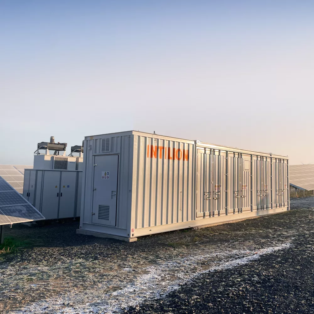 Große, hellgraue, modulare Container-Energieanlagen mit der Aufschrift INTILION inmitten von Solarzellen.