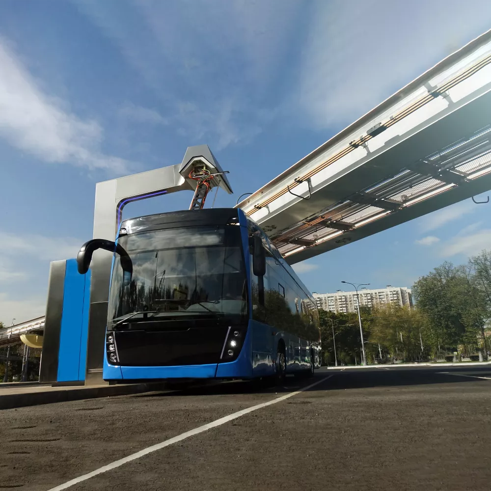 Blauer Elektrobus an einer Ladestation unter einer hochgelegenen Fußgängerbrücke.