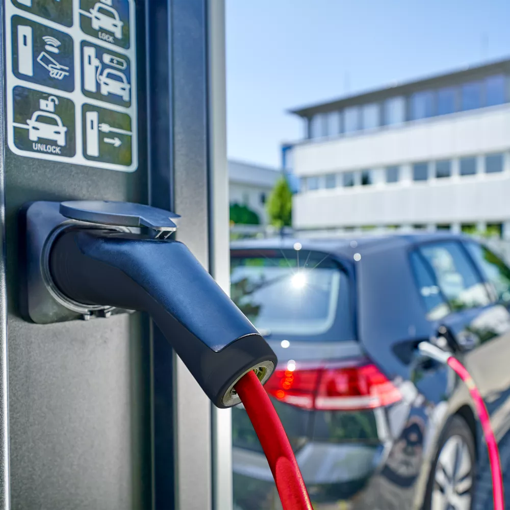 Ladestation für Elektrofahrzeuge mit einem roten Ladekabel, das an ein dunkelgraues Auto angeschlossen ist.