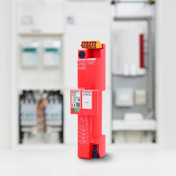 Im Vordergrund ist ein rotes elektronisches Gerät mit verschiedenen Anschlüssen zu sehen, im Hintergrund sind unscharfe elektrische Komponenten zu sehen.
